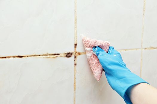 A woman cleans a tiled wall tile from mold with a foam detergent.