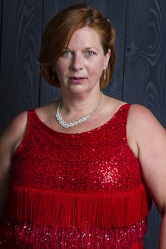 forty something brunette woman wearing a red sparkling dress in front of blue wood panel