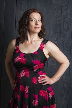 forty something brunette woman wearing a summer dress in front of a wood panel