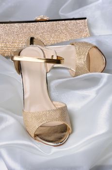 A pair of gold sandals with a high heel, with a golden clutch on the table