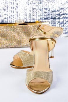 A pair of gold sandals with a high heel, with a golden clutch on the table
