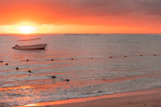 Fishing boat anchored near the shore of the beach at orange sunset,mauritius beach Flic and Flac.