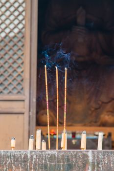 Burning incense at a stone alter in front of a temple housing a giant wooden sculpture of Buddha.