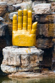 Close up of a giant golden 'Buddha's Palm" statue under a waterfull under restoration.