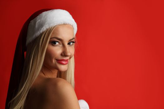 Portrait of a happy attractive young woman posing in red santa claus costume on red background with copy space