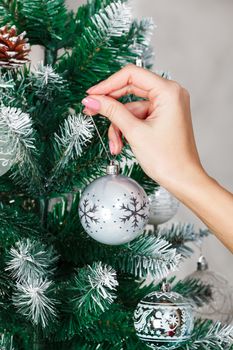 Woman's hand hanging silver Christmas ball on fir tree, holiday concept