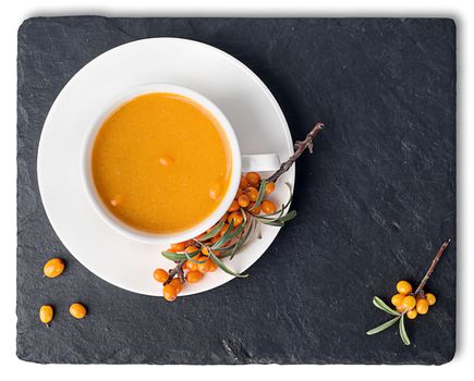 Tea of sea-buckthorn on a black slate stone. A branch of sea-buckthorn. White cup is a top view. Isolated on white background.