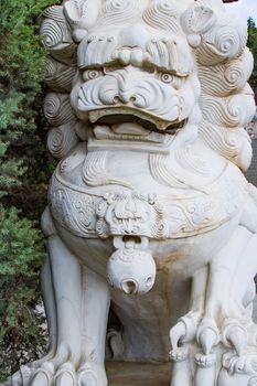 A large, white Chinese lion carved into a white rock guards the entrance to a temple