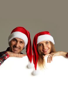 Happy couple in Santa hats holding blank banner with white copy space