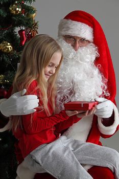 Portrait of smiling little girl sitting on santa claus knees and getting small gift