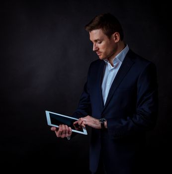 Young handsome businessman using digital tablet, studio shot on dark background