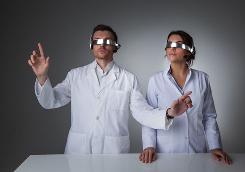 Two scientists or doctors using futuristic VR goggles headset with microphone and touching virtual screen