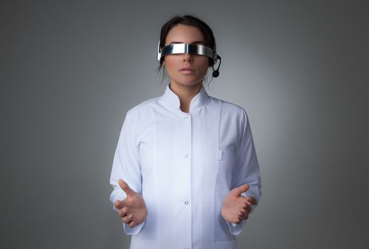 Female scientist or doctor using futuristic VR goggles headset with microphone and holding virtual object