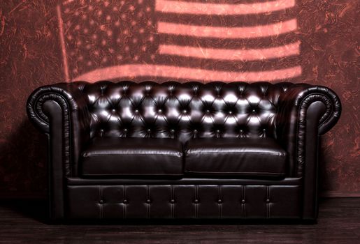 Vintage old dark brown leather sofa with grunge brown wall with the USA flag in the living room