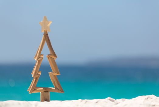 Timber Christmas tree with star sits in pristine white sand with idyllic beach background.  A summer Christmas.  