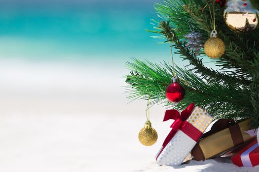 Christmas time spent at the beach in summer. A christmas tree surrounded by presents on a beautiful sandy beach.  Shallow dof with space for copy