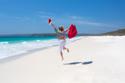 Celebrating Christmas in Australia, hot sunny days and lazy days down at the beach.  A woman jumps for joy on a beautiful stretch of white sandy beach.  Christmas celebration, Christmas vacation, space for copy