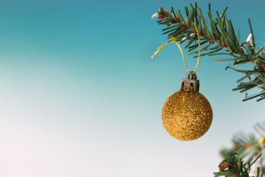 Gold glitter b auble on Christmas tree with beautiful beach background blur.