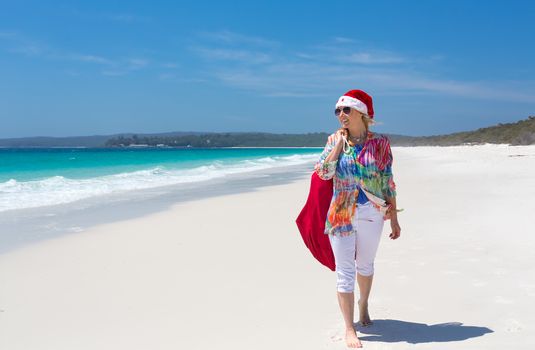 Hot summer days Christmas down on the beach or summer vacation southern hemisphere.  A casually dressed female strolling along the beach wearing a red santa hat.