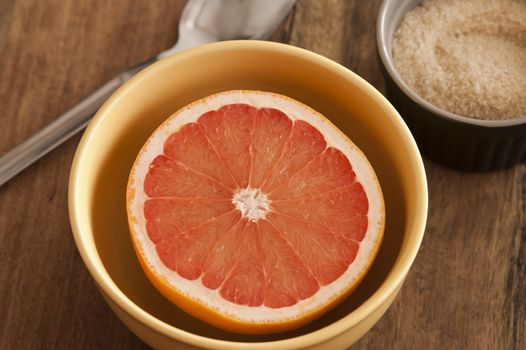 Cut fresh juicy pink grapefruit served for breakfast in a bowl with accompanying sugar for a healthy diet rich in vitamin C