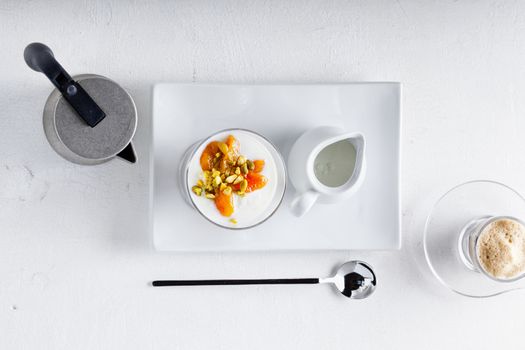 Yogurt with dried apricots and coffee on a white surface
