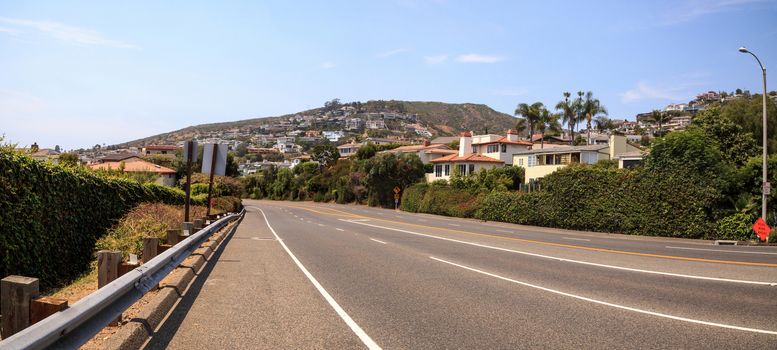 Blue sky over Pacific Coast Highway road heading into Laguna Beach with beautiful homes along the hillside.