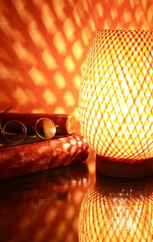 Nice wicker glowing desk lamp near old book against red wall