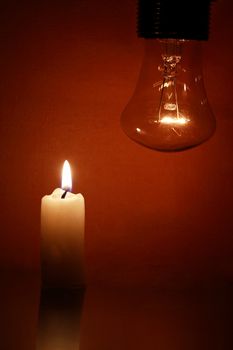 Closeup of glowing light bulb near lighting candle