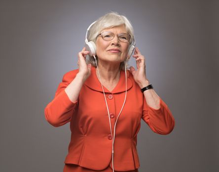 Smiling senior lady with headphones on listening to the music on gray background