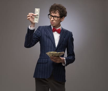 Happy smiling man in a suit holding fan of dollar banknotes on gray background