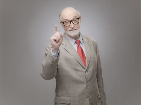 Senior man points finger up on gray background with copy space