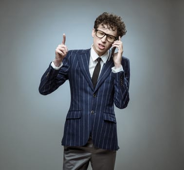 Young man calling on phone with finger up on gray background