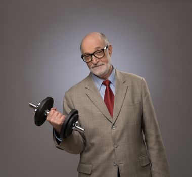 Happy funny senior man in suit with dumbbell, power concept