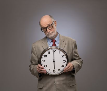 Studio portrait of a senior man holding a big wall clock on gray background with copy space