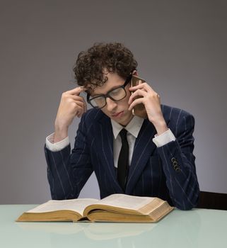 Man in suit and glasses reading book and calling on mobile phone