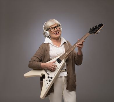 Happy funny senior woman playing electric guitar