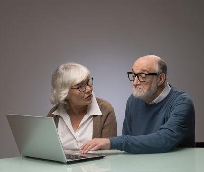 Ssenior couple looking at a laptop together, studio shot on gray background with copy space