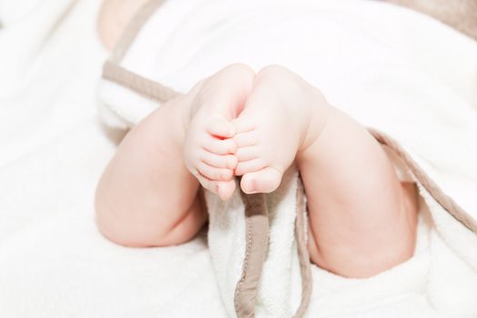 Baby legs on the bed, soft focus newborn tiny feet, lower body. Close up picture of new born baby feet on a white sheet.