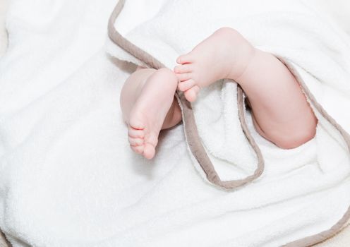 Baby feet under the towel.Baby lying in diaper on the bed, unrecognizable baby.Shallow doff. Close up picture of new born baby feet on a white sheet.