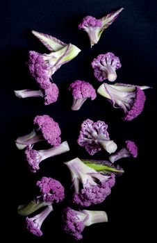 Arrangement of Fresh Raw Purple Sprouts of Cauliflower with Leafs isolated on Black background. Top View