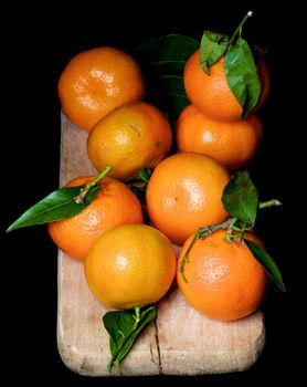 Fresh Ripe Tangerines with Leafs and Stems on Wooden Cutting Board isolated on Black background