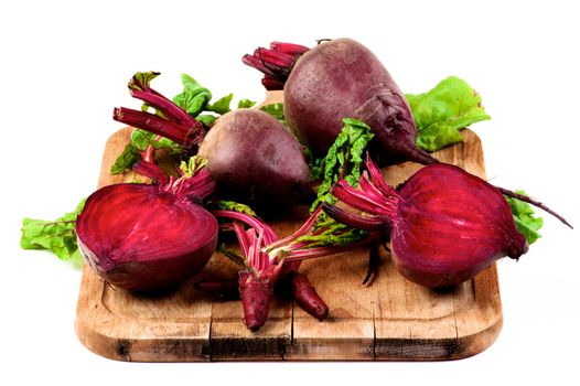 Arrangement of Fresh Raw Organic Beet Roots Full Body, Halves and Young Sprouts with Green Beet Tops closeup on Wooden Cutting Board isolated on White background