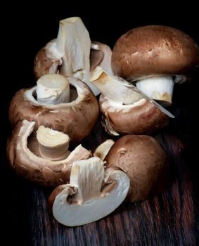 Arrangement of Fresh Raw Portobello Mushrooms Full Body and Slices closeup on Dark Wooden background. Focus on Foreground