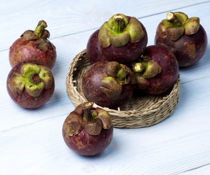 Stack of Fresh Ripe Mangosteen in Wicker Bowl closeup on Light Blue Wooden background