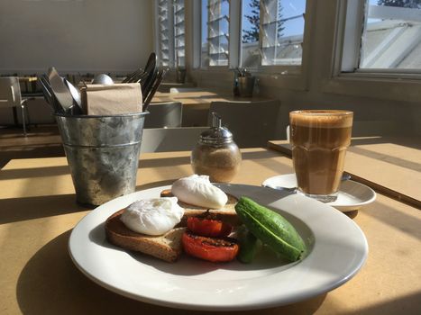Breakfast time, poached eggs on toast with sliced avocado and char grilled tomato.  A latte in a glass with glorious sunlight streaming in through the windows
