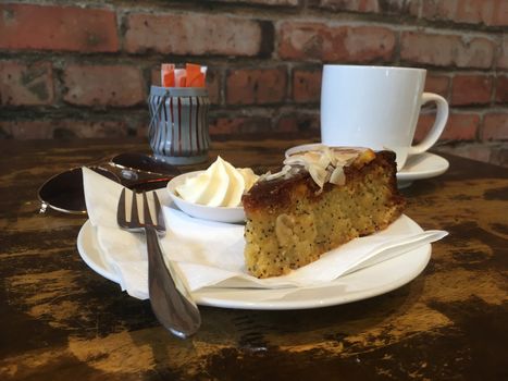 Morning tea break in a cafe.  Orange and poppyseed cake with a side of cream with a capuccino