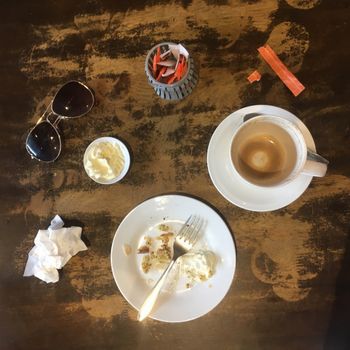 After Shot.   Top View of the remains of a table after finishing a slice of gluten free orange and poppyseed cake with a side of cream and a coffee in a mug in a rustic cafe.  Be sure to check out  my before shot.