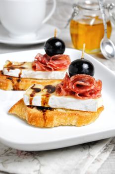 Snack from a toasted slice of baguette with soft under a noble white mold Cheese Brie, salami, a berry of grapes with honey