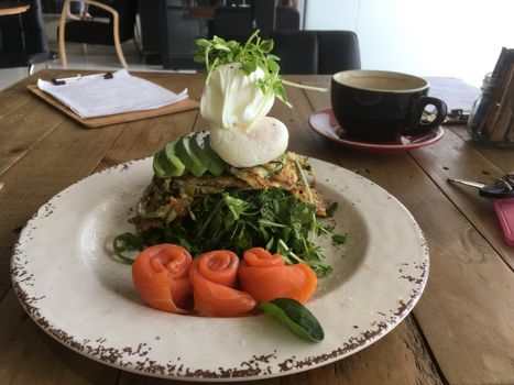 Gluten free zucchini sweet potato fritters with poached eggs and avocado and rolled smoked salmon on a table in a wellness cafe