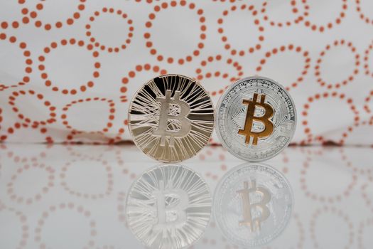 Digital currency physical gold and silver bitcoins on the white and orange scene.